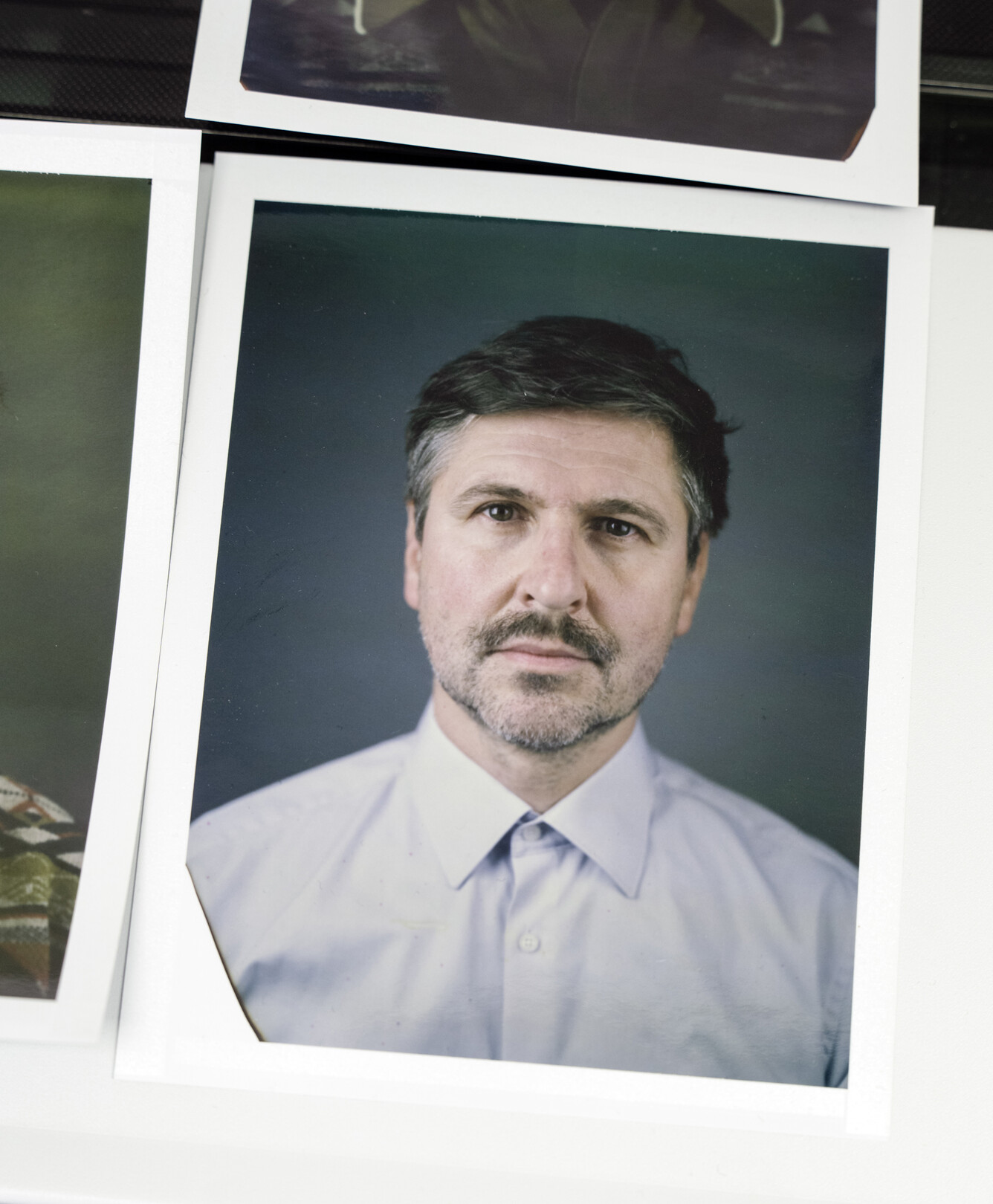 Auf dem Bild ist ein Polaroidbild zu sehen, auf dem Christian Kleiner abgebildet ist, der ein weißes Hemd trägt und ernst in die Kamera schaut.