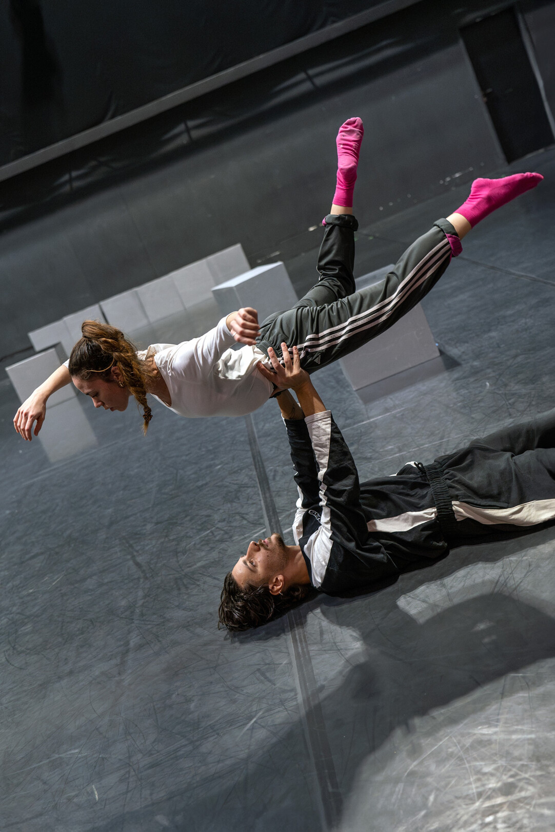 Zwei Personen in Sportkleidung führen eine Akrobatikübung auf einer Bühne aus, eine liegt auf dem Rücken und hält die andere waagerecht in der Luft.